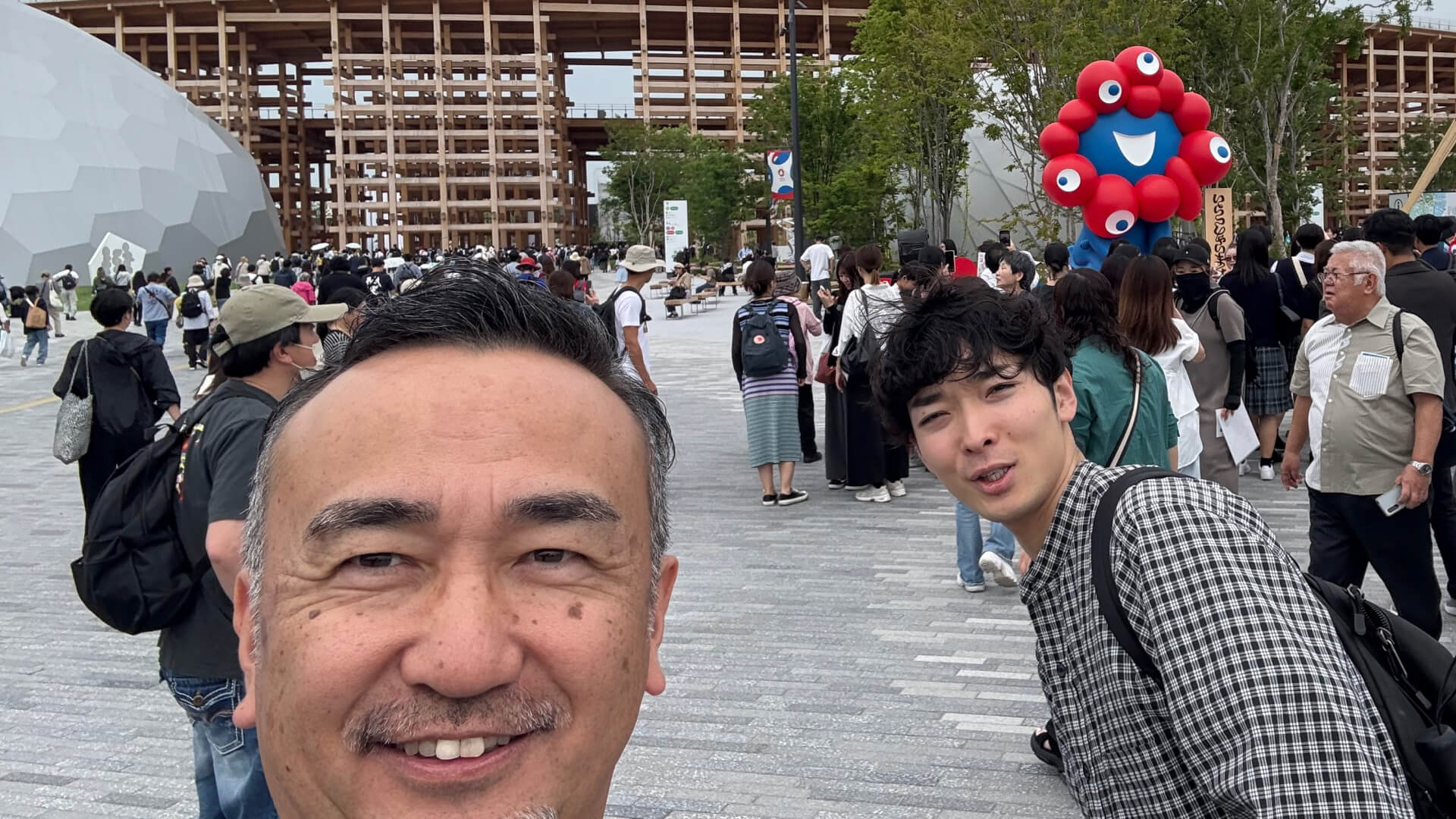 万博会場を背景に男性二人が楽しそうにしている写真